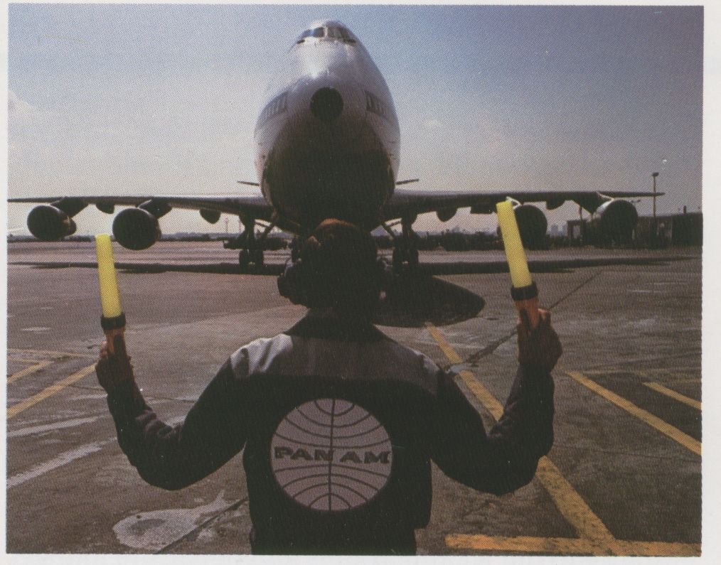 1983 April, A Pan Am Mechanic guides a 747 to a ramp parking spot.